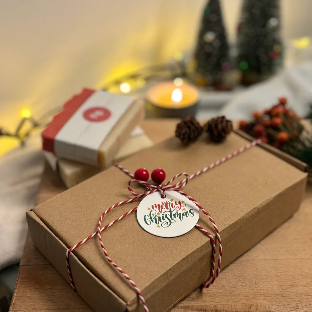 Christmas gift box with organic soaps, a lit candle and christmas decorations in the background
