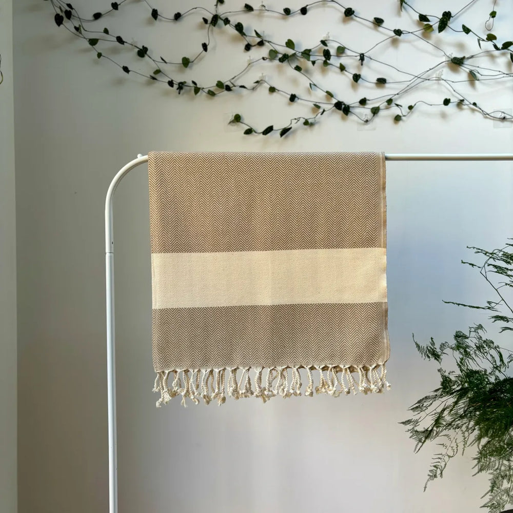 100% organic cotton herringbone patterned brown and white Turkish Towel hanging on a clothes rack surrounded by plants on a white background