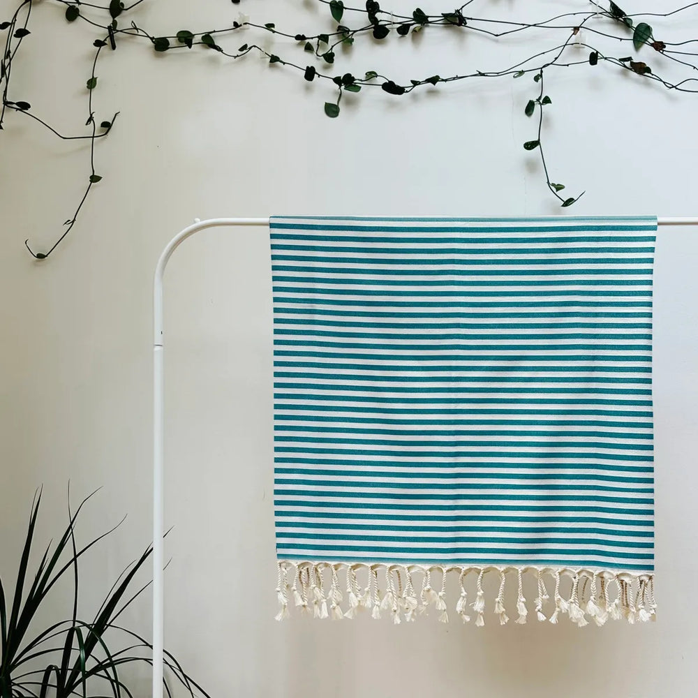 100% organic cotton stripy blue and white Turkish Towel hanging on a clothes rack surrounded by plants on a white background