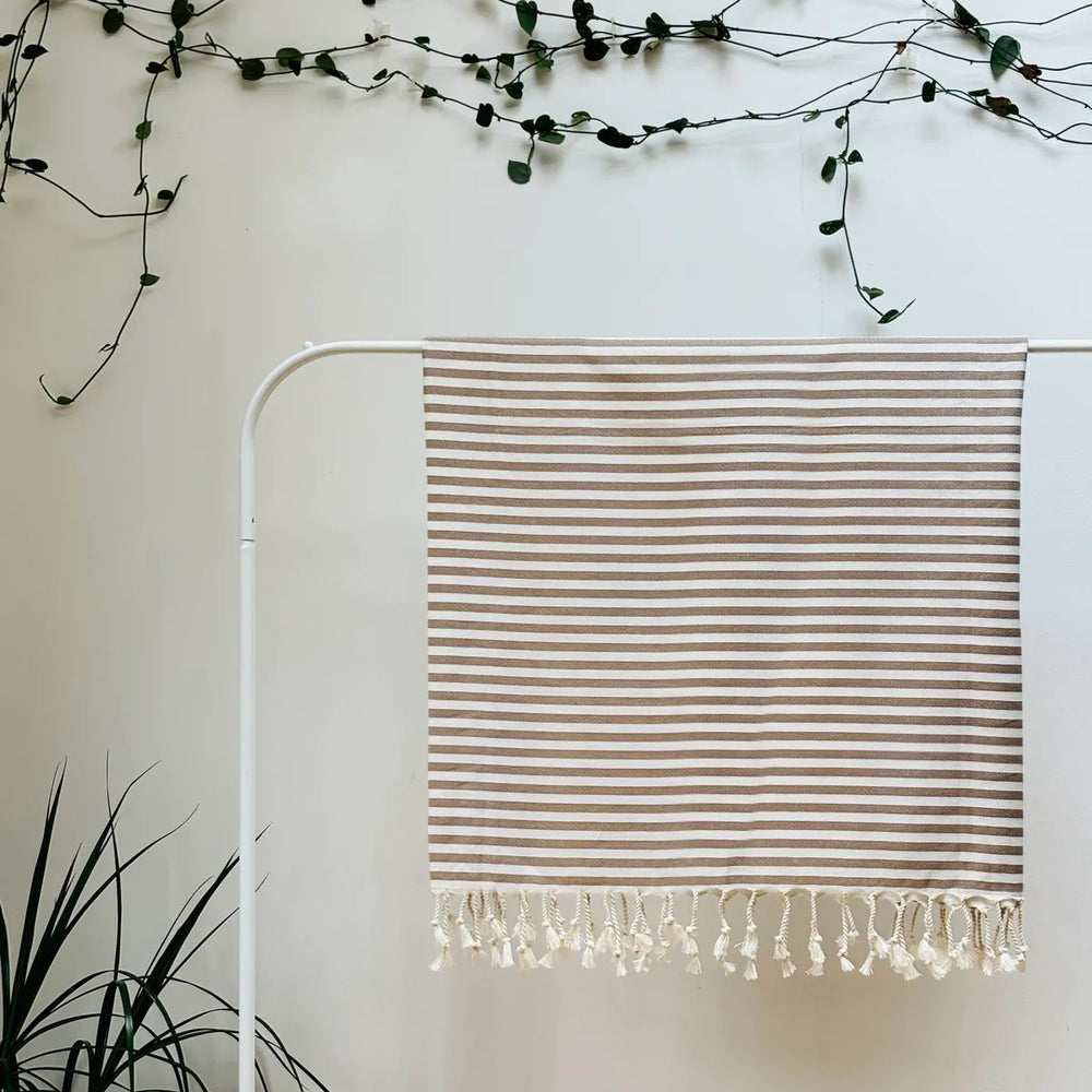 100% organic cotton stripy brown and white Turkish Towel hanging on a clothes rack surrounded by plants on a white background