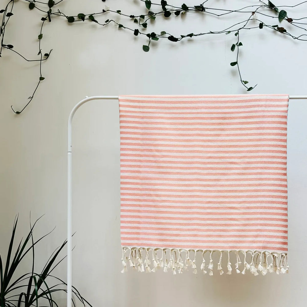 100% organic cotton stripy peach and white Turkish Towel hanging on a clothes rack surrounded by plants on a white background