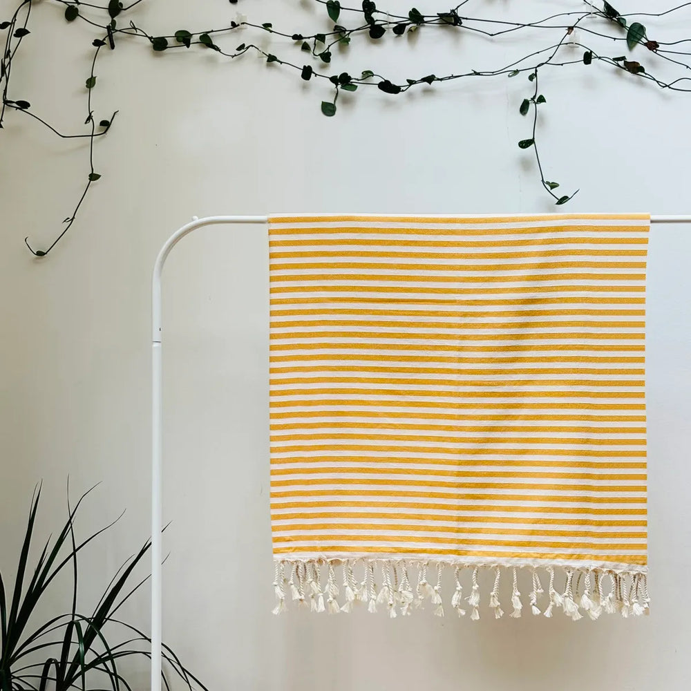 100% organic cotton stripy yellow and white Turkish Towel hanging on a clothes rack surrounded by plants on a white background