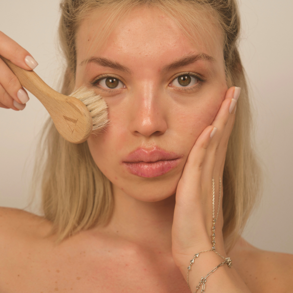 Woman holding a wooden brush near her face with a plain background