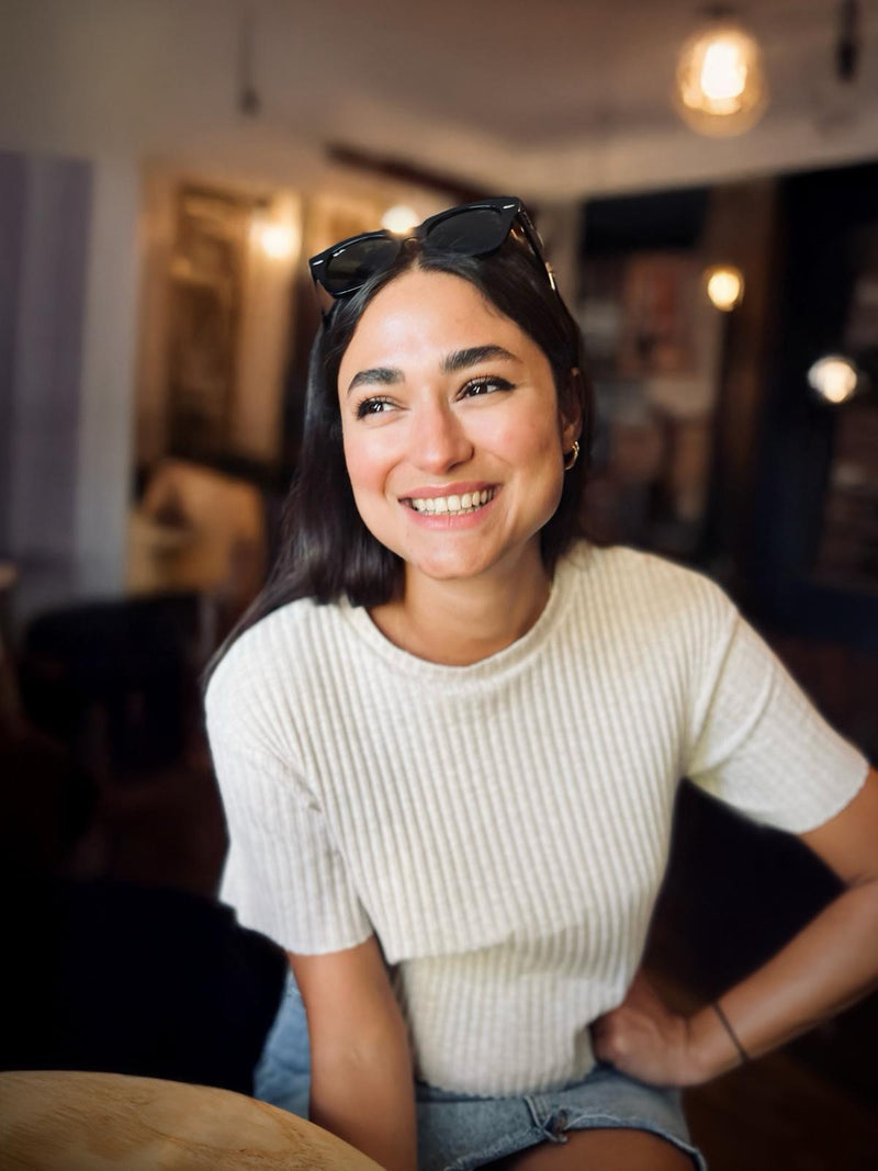 Woman wearing a white sweater and denim shorts sitting indoors.
