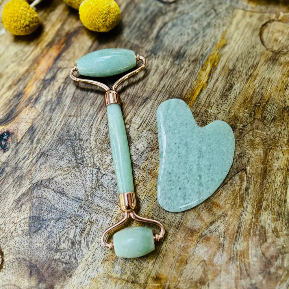 Jade facial roller and gua sha tool on a wooden surface with yellow flowers.