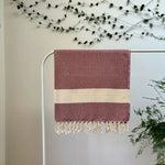 100% organic cotton diamond patterned cherry and white Turkish Towel hanging on a clothes rack surrounded by plants on a white background