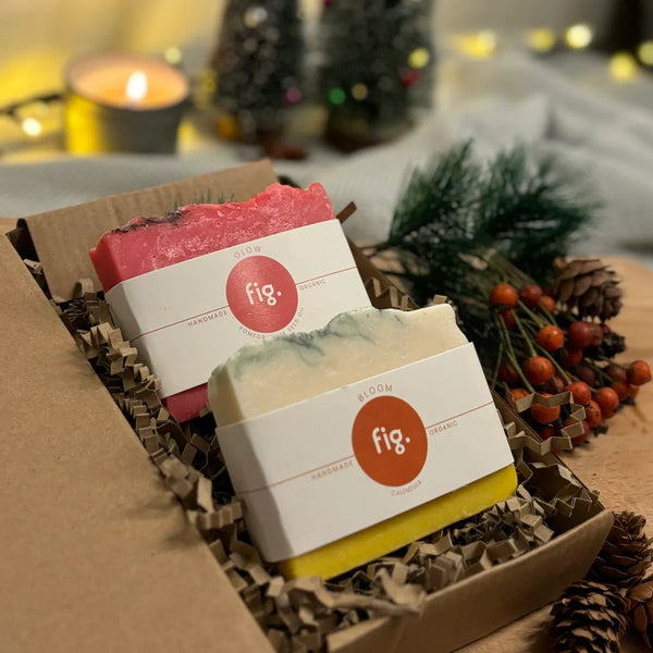 Two organic soaps. with belly bands on display in their gift box with a lit candle and christmas decorations in the background