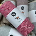 100% organic cotton herringbone patterned Turkish Towel in pink colour on a table with different coloured towels
