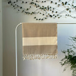 100% organic cotton herringbone patterned brown and white Turkish Towel hanging on a clothes rack surrounded by plants on a white background