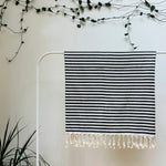 100% organic cotton stripy black and white Turkish Towel hanging on a clothes rack surrounded by plants on a white background