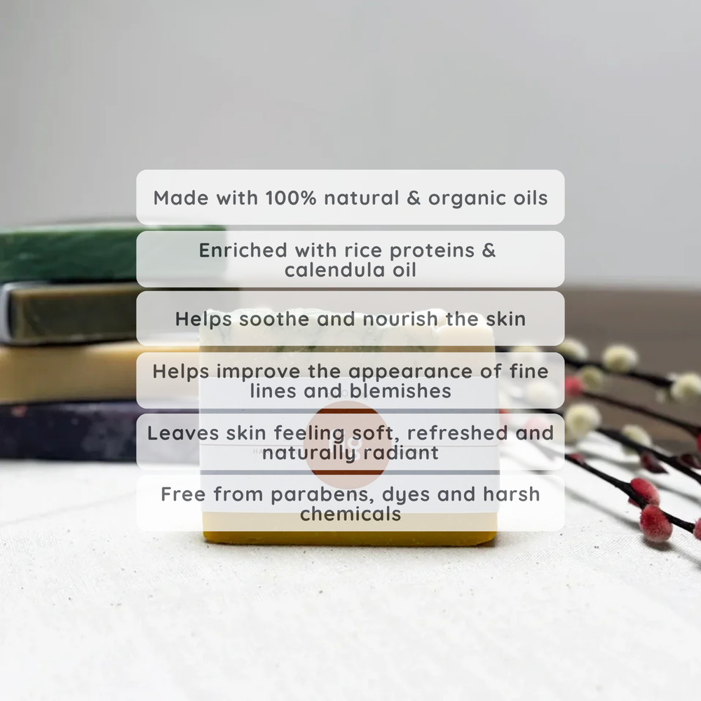 A small rectangular skincare bottle or jar with a white cap and a warm golden-yellow body sits on a light surface with blurred books and decorative branches in the background. Six translucent text boxes overlay the center, listing benefits such as natural organic oils, rice protein and calendula oil, soothing effects, and free from parabens and harsh chemicals.