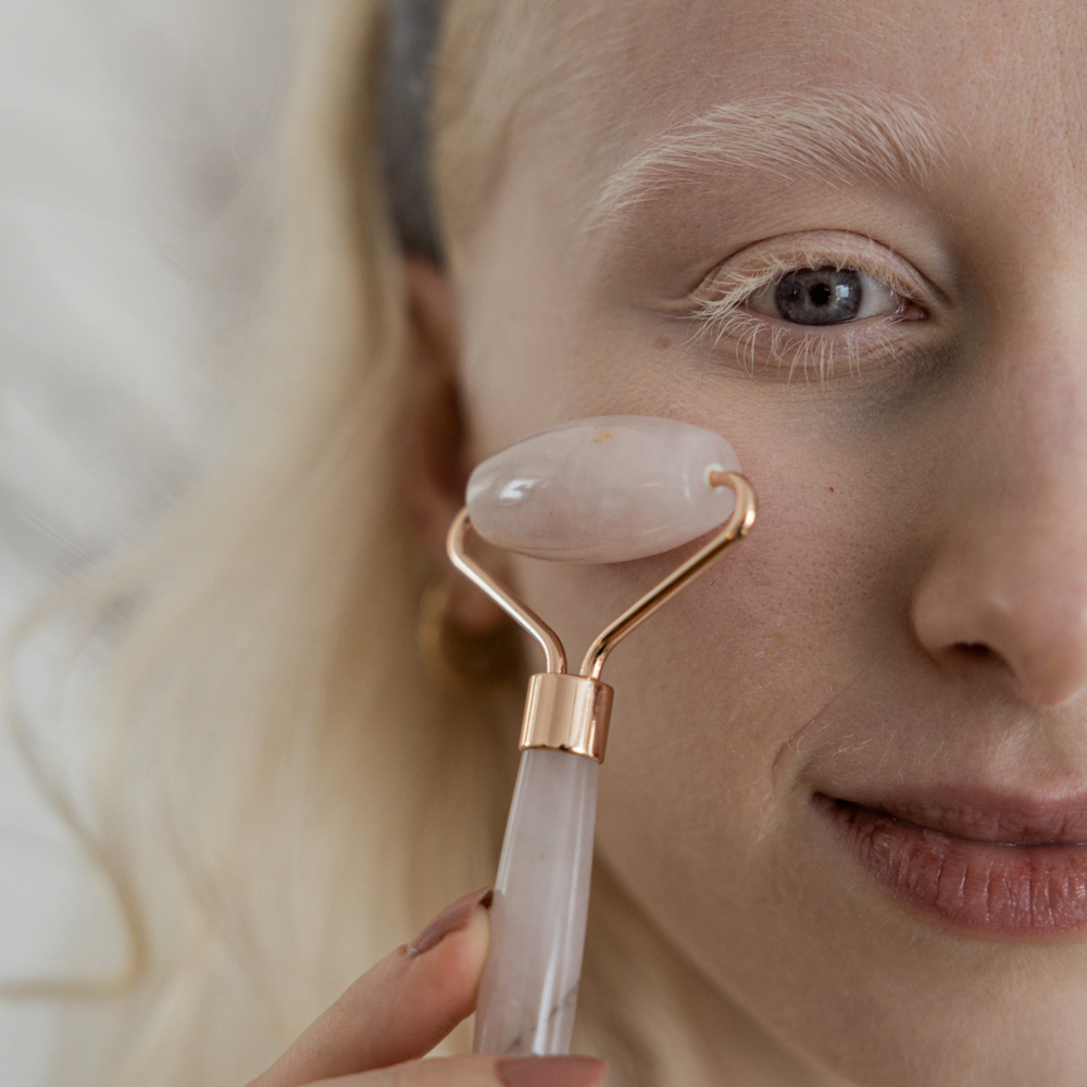 Person using a facial roller on their face with a neutral background