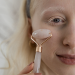 Person using a facial roller on their face with a neutral background