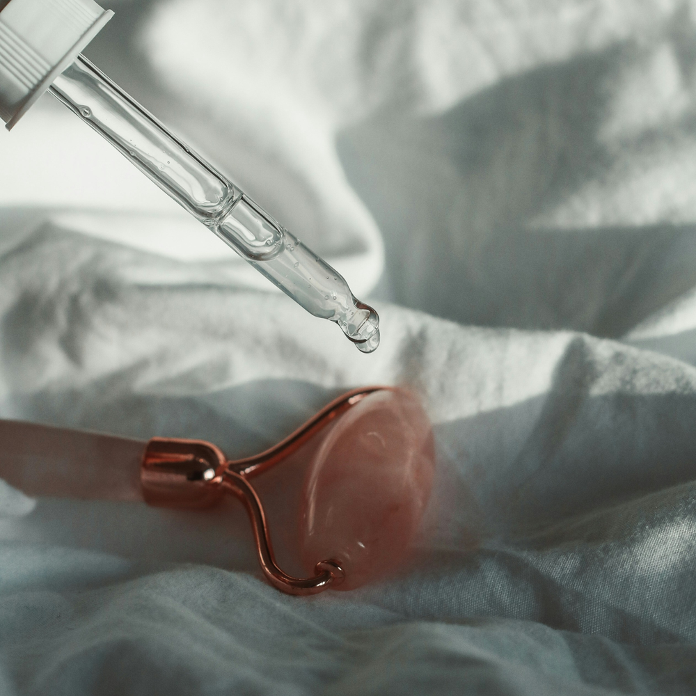 Dropper with clear liquid next to a pink roller on a light fabric background