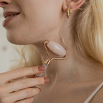 Woman using a jade roller on her face with a neutral background