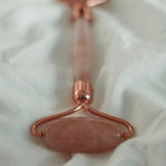 Rose gold facial roller on a white fabric background