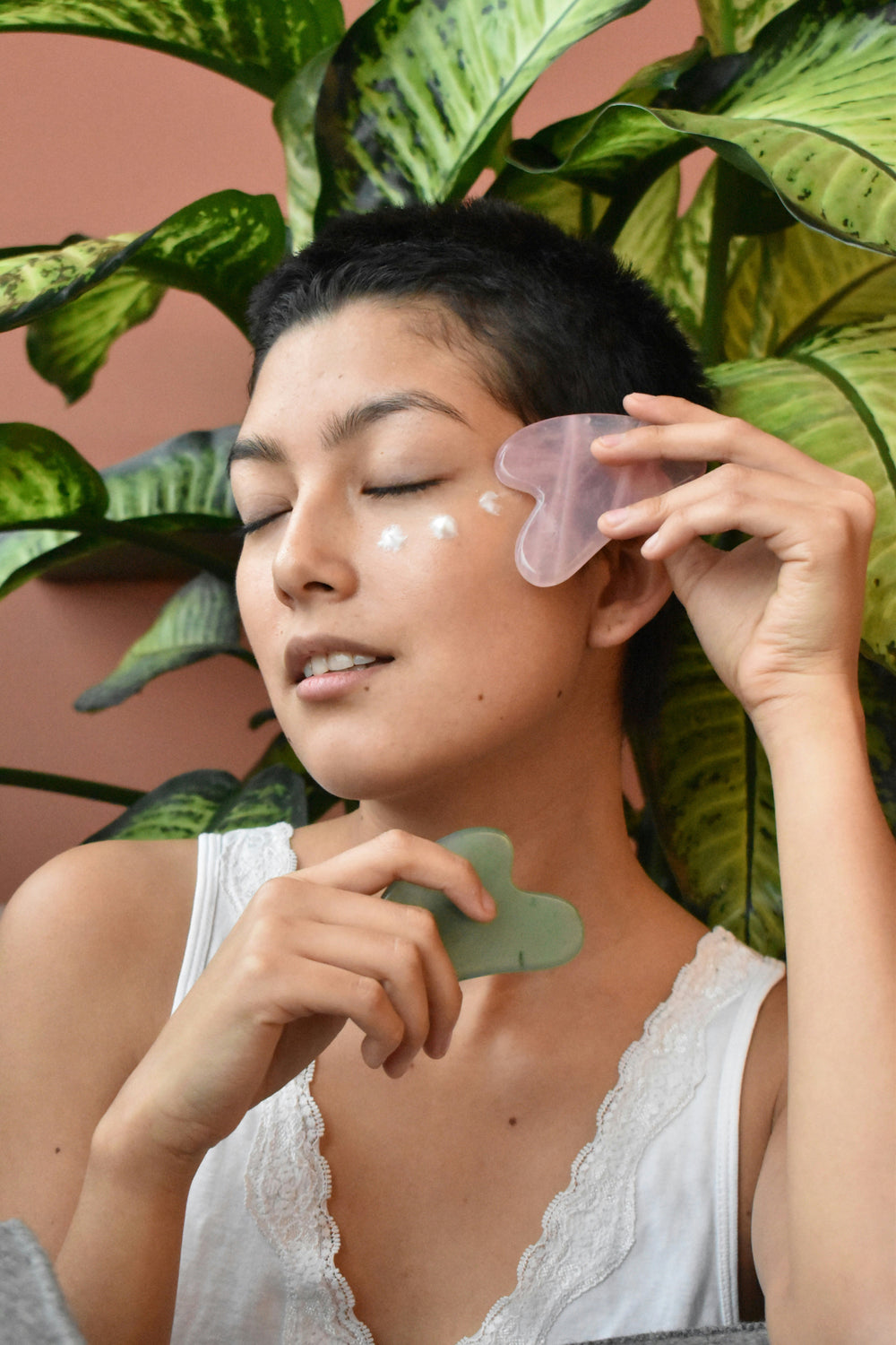 Woman using a gua sha tool on her face with plants in the background