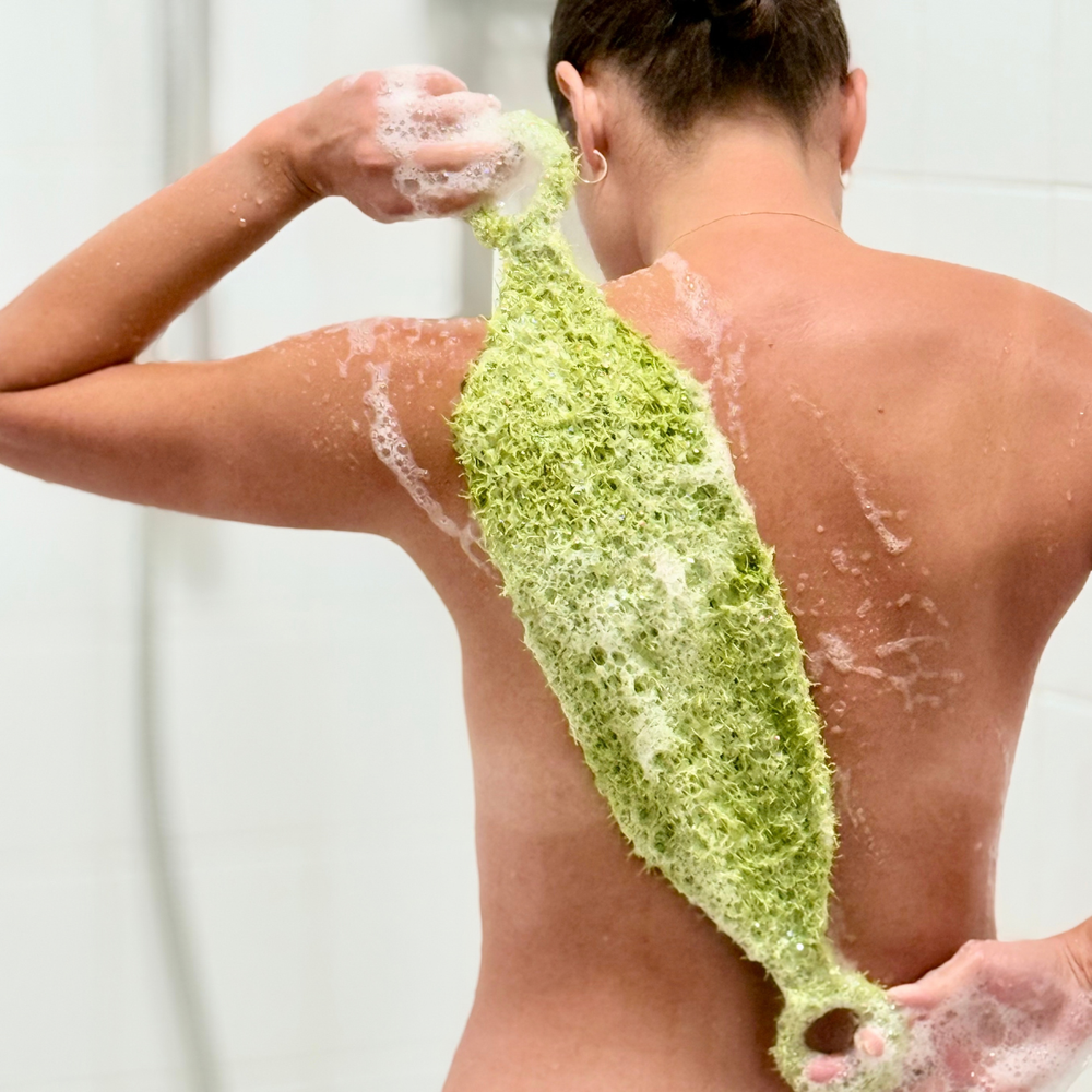 a woman using a loofah or shower mitt to scrub, exfoliate her back