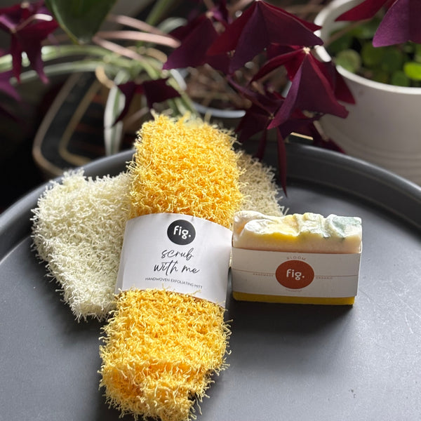 yellow scrub and a bar of soap on a gray surface with plants in the background.