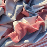 A close-up of draped striped fabric with alternating bands of dusty pink, light blue, and off-white, showing a fine woven texture under natural sunlight.