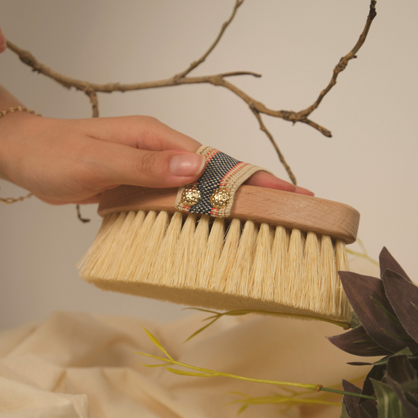 Hand holding a cactus bristle dry body brush with a neutral background